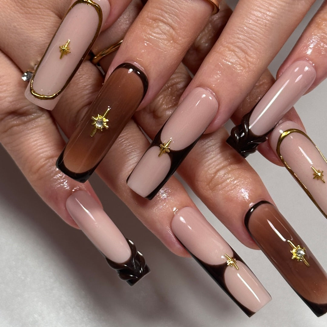 Close-up of hands with long, multicolored nails featuring gold star decorations on a neutral background.