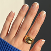 Hand wearing a gold ring with a blue sleeve against a neutral background