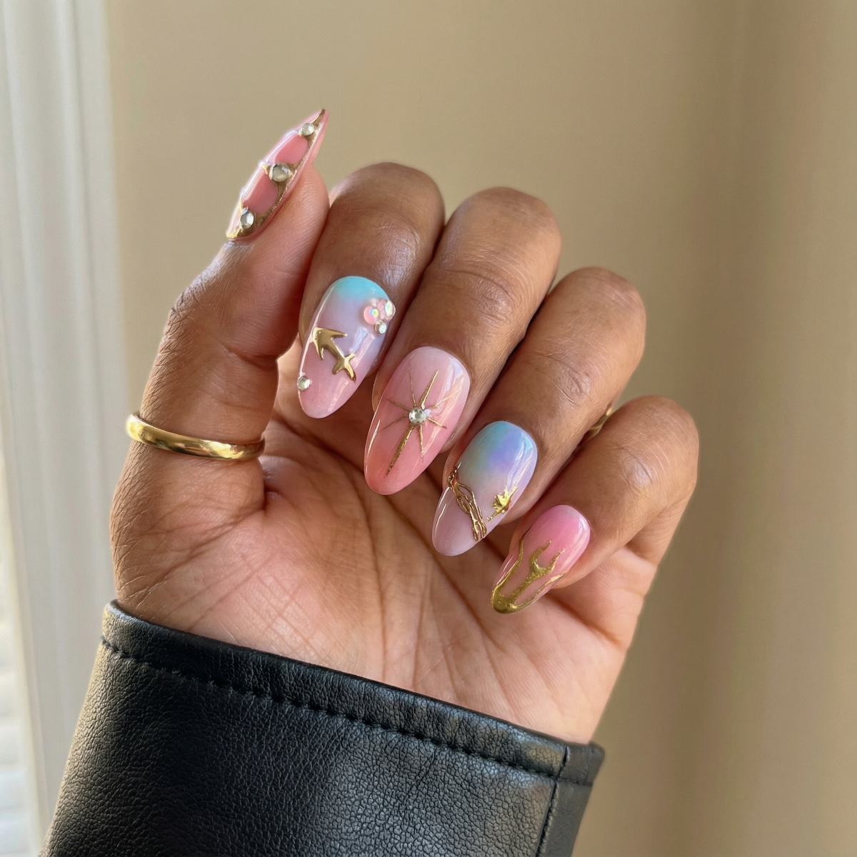 Hand with pastel nail art featuring flowers and gold accents on a neutral background