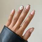 Hand with manicured nails featuring a floral design on a neutral background