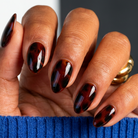 Hand with tortoiseshell nail polish wearing a blue sleeve against a dark background
